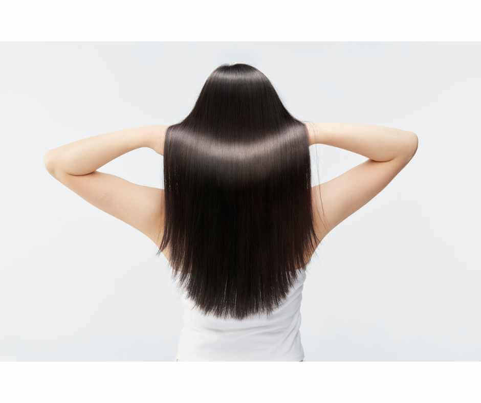 Woman with long healthy shiny hair shown from the back after microneedling treatment for hair loss.