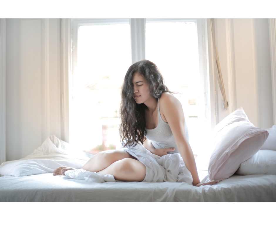Woman experiencing abdominal pain and bloating related to gluten intolerance and digestive inflammation while sitting on a bed